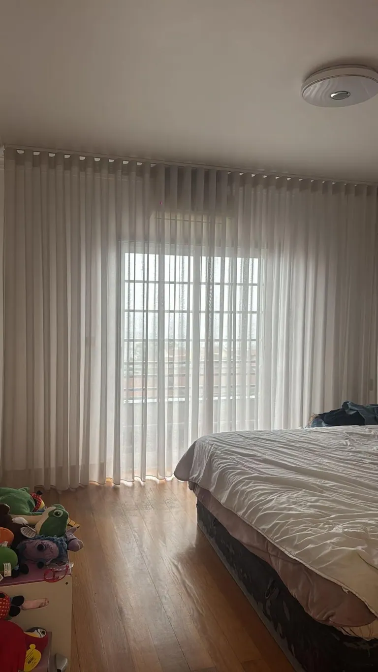 Cortinados em onda a cobrir a porta de varanda de um quarto, com queda até ao chão